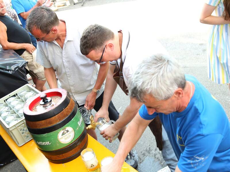 Drei Männer zapfen Bier aus einem Fass in Gläser während einer Veranstaltung im Freien.