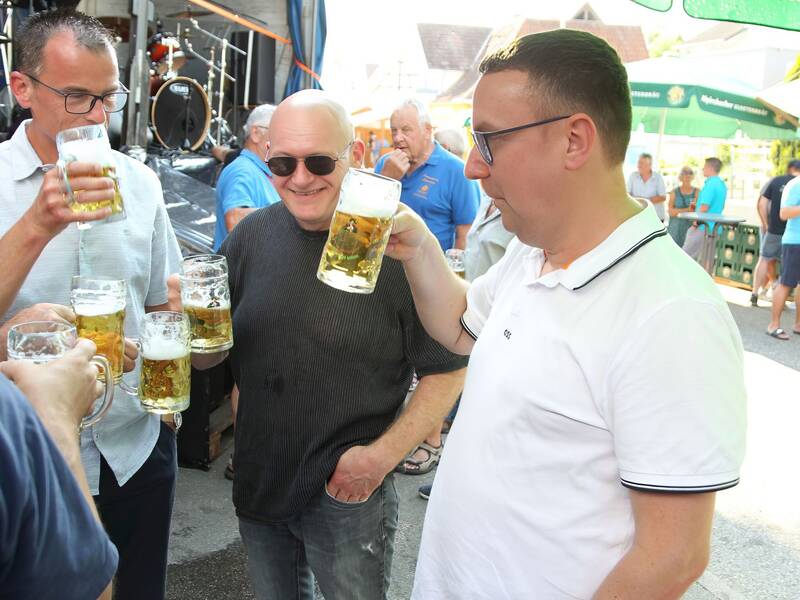 Mehrere Menschen stehen im Freien zusammen und trinken Bier aus großen Krügen.