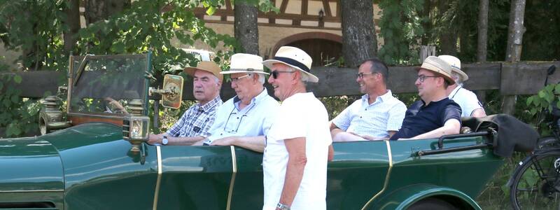 Eine Gruppe von Männern sitzt in einem grünen Oldtimer, während ein weiterer Mann davor steht.