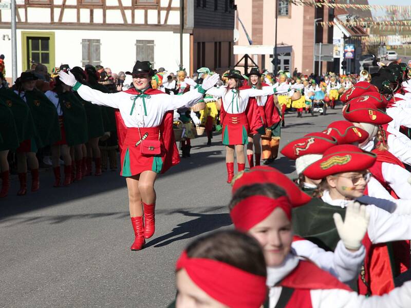 Eine Gruppe von Menschen in bunten Kostümen und traditionellen Hüten marschiert in einer Parade durch eine belebte Straße.