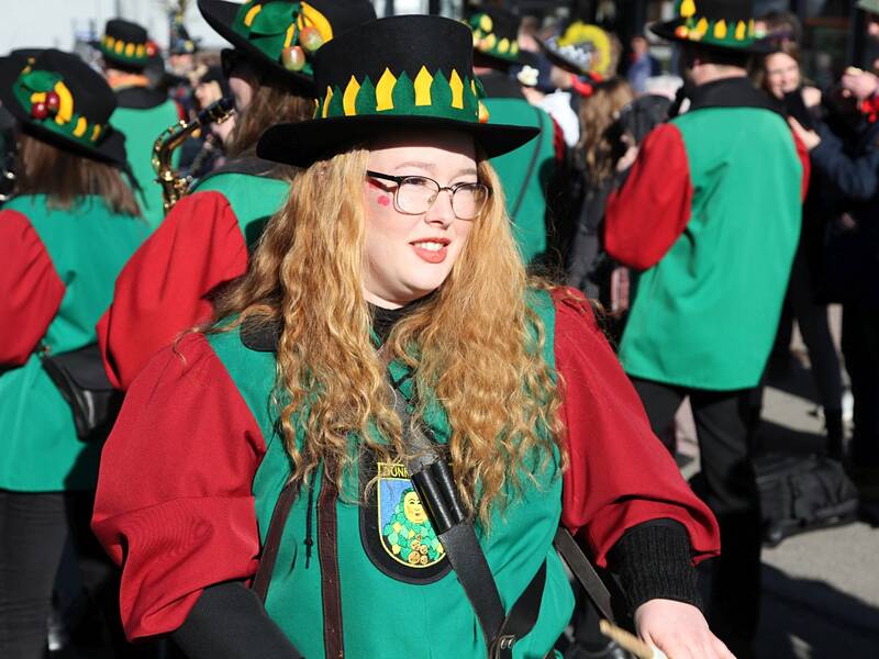 Eine Frau in einem farbenfrohen Kostüm mit Hut marschiert in einer Gruppe während einer Parade.