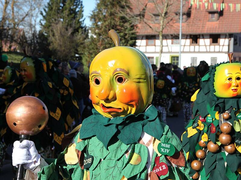 Menschen tragen leuchtend gelbe Masken und Kostüme mit grünen Blättern, während sie an einem Umzug teilnehmen.