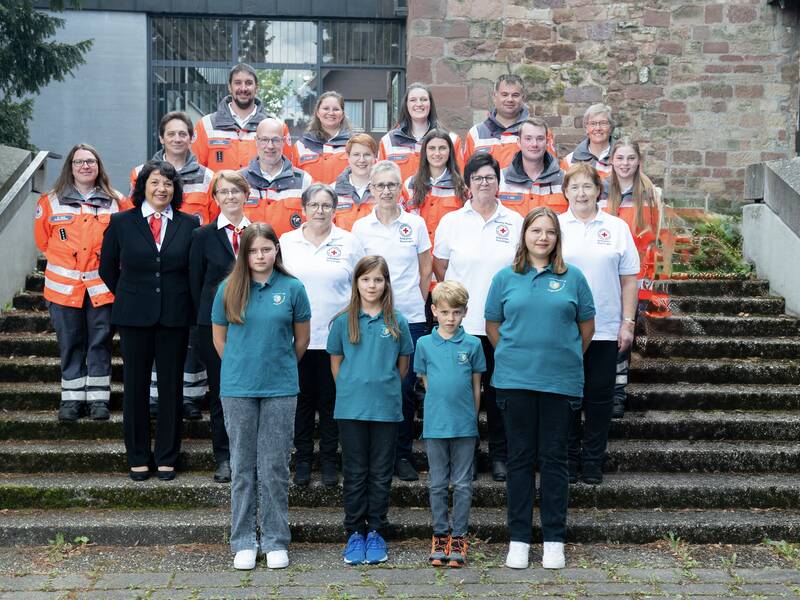 Eine Gruppe von Menschen, einige in orangenen und einige in weißen oder blauen Uniformen, steht auf einer steinernen Treppe.