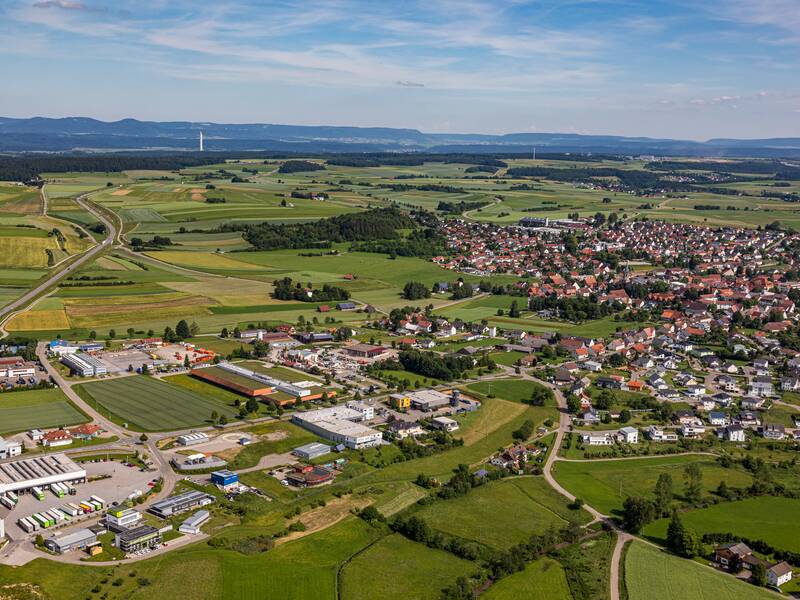 Luftaufnahme einer ländlichen Gegend mit einer kleinen Stadt, umgeben von grünen Feldern und Straßen, die durch die Landschaft führen.